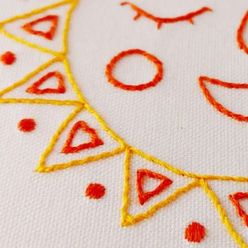 Detail eines handgestickten Sonnenbildes - leuchtend gelbe Fäden auf weißem Leinen